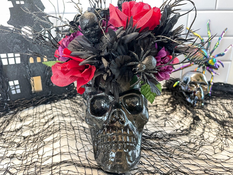 A black skull vase with black and red flowers inside sitting alongside other Halloween decor.