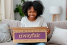 a woman sitting on a couch opening a wayfair box 