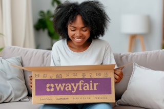 a woman sitting on a couch opening a wayfair box 