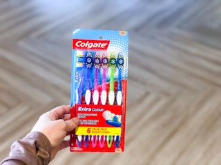 A hand holding a pack of six Colgate Extra Clean Toothbrushes.