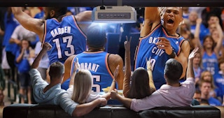 A group of people watching a basketball game projected onto a wall.