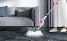 a person mopping under a couch with a pink and white steam mop