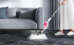 a person mopping under a couch with a pink and white steam mop