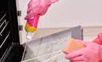 a person cleaning an oven with a pink bottle of cleanser