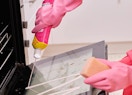 a person cleaning an oven with a pink bottle of cleanser