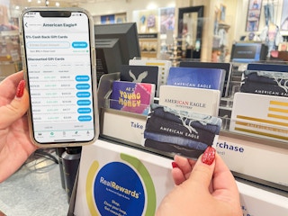 a person holding up a american eagle gift card next to a cellphone with raise app on screen 