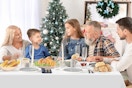 A family gathers around a table covered with a white plastic tablecloth. Plates of food, utensils and candles are arranged on it