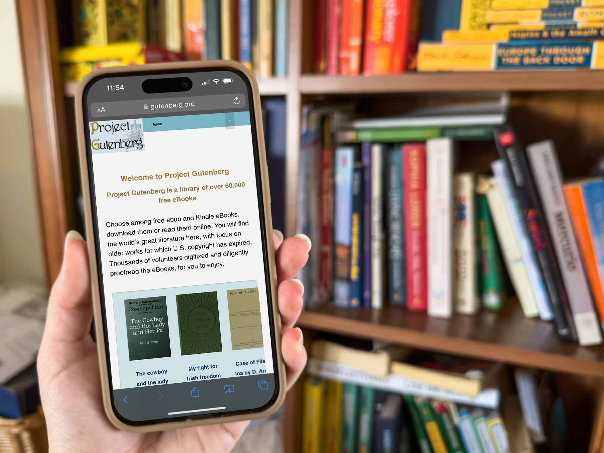 Someone holding a cell phone displaying the Project Gutenberg website in front of a shelf of books