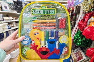 person holding a sesame street backpack in an aisle
