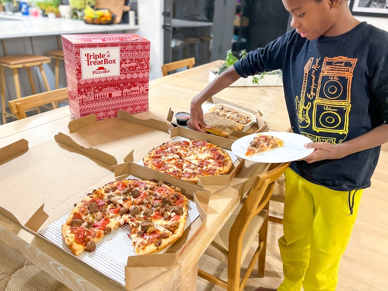 A young boy taking a slice of pizza from a box on a table