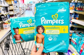 hand holding pack of pampers diapers in store aisle above shopping cart