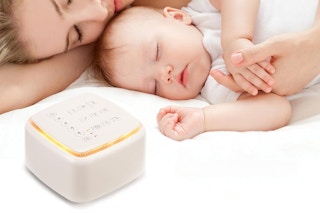 A mother and baby sleep on a white sheet next to the white noise machine, which has a soft light.