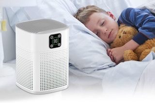 A rectangular white air purifier suitable for 600 square feet sits next to a sleeping boy and does not wake him.