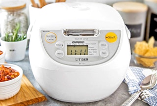 tiger rice cooker on a counter top surrounded by food in glass bowls
