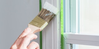 A hand painting a wall against Frogtape painter's tape