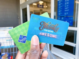 Sam's Club membership card and Sams club gift card being held in hand in front of Sams club entrance