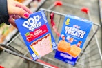 person placing a box of pop tarts in a cart with rice krispies treats