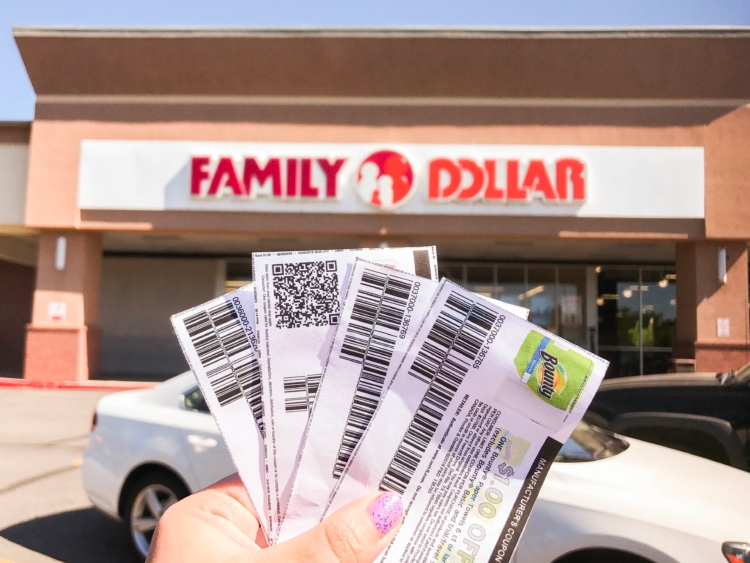 Hand holding up printed Family Dollar coupons in front of a Family Dollar store