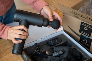 hand holding muscle massage gun by an amazon box