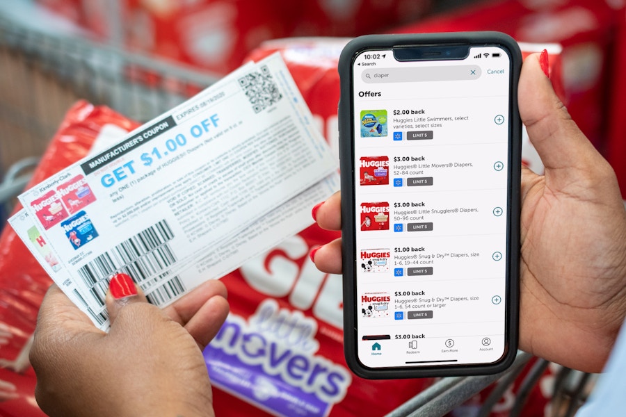 Ibotta app on a cell phone next to coupons and Huggies diapers.