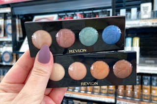 hand holding two revlon illuminance eyeshadow palettes in front of a revlon cosmetics display