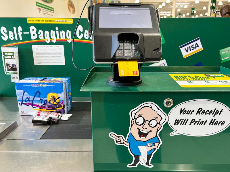 A credit card in a point of sale machine in the checkout lane at Menards with products on the conveyer belt.