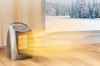 A space heater sits in the corner of a room blowing hot air around. A snowy woods is visible out the window.