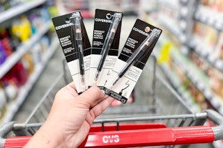 hand holding three covergirl eyeliner pencils next to a cvs shopping cart