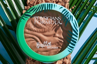 bronzer in a green compact on a palm leaf