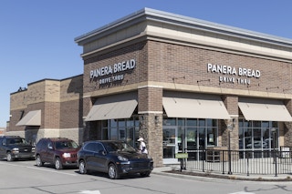 The outside of a Panera Bread with a line of cars going through the drive thru