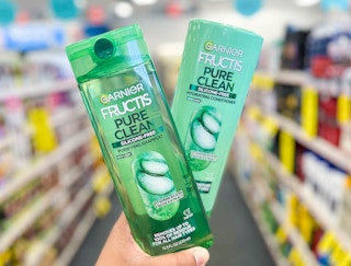 hand holding one bottle of Garnier Fructis Shampoo and Conditioner in aisle