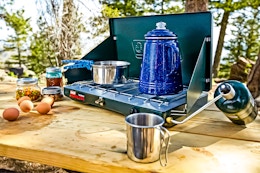 Lifestyle image of the Coleman 2-Burner Propane Stove being used outdoors to cook up a meal