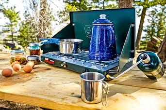 Lifestyle image of the Coleman 2-Burner Propane Stove being used outdoors to cook up a meal