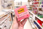 hand holding a pack of pink post-it notes