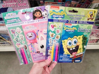 hand holding up a gabby's dollhouse activity book and a spongebob activity book