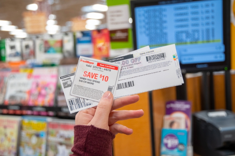 A person holding up printed coupons in front of a checkout register.