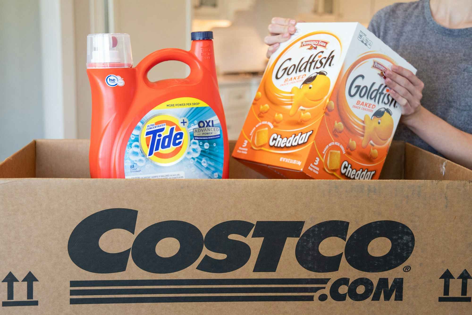 A person pulling gold fish crackers and tide from a Costco.com shipping box.