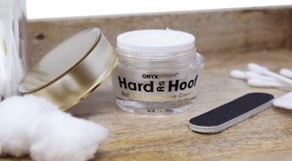 a jar of cream on wood next to a nail file and cotton balls and swabs