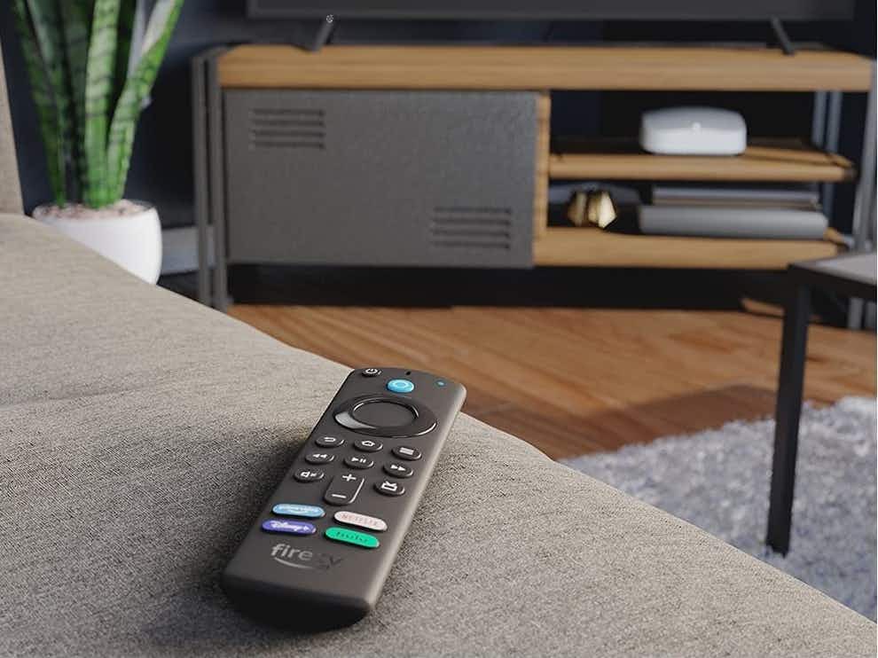 An Amazon Fire TV remote on a couch, pointing toward a TV.