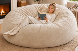Lifestyle image of a woman sitting in a beige color large bean bag chair