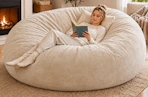 Lifestyle image of a woman sitting in a beige color large bean bag chair