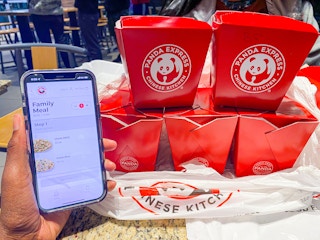 someone holding a phone next to a family Panda Express meal