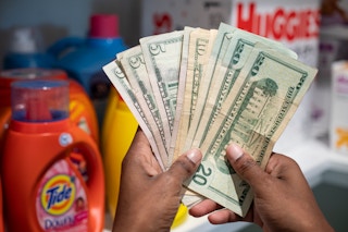 A person holding a stack of cash in front of a stockpile or brand name products in a storage room
