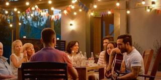 A group of people eating below outdoor string lights