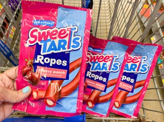 hand holding a sweetarts ropes bag with two in walmart cart