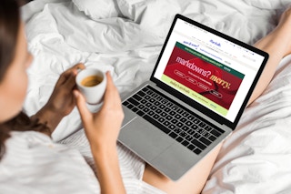 a woman sitting on her bed drinking coffee and shopping online at Marshalls on her laptop