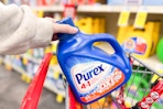 person placing a large bottle of purex detergent in a cart
