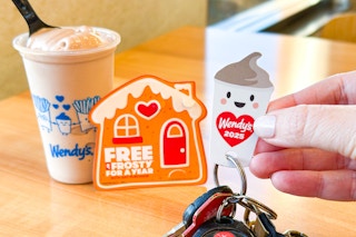 a hand holding a wendy's frosty key tag next to a frosty on a table 