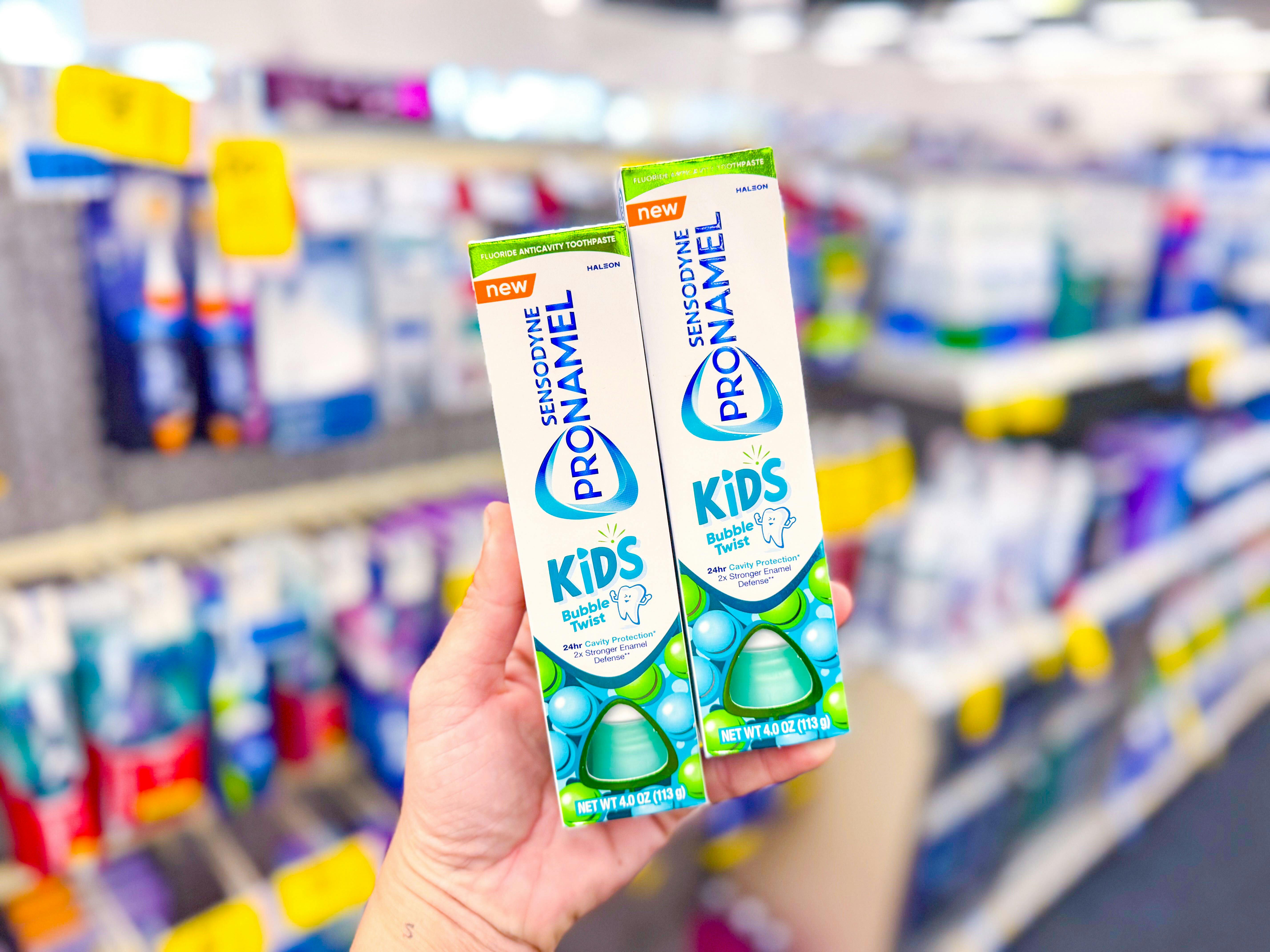 person holding 2 tubes of sensodyne kids toothpaste in an aisle