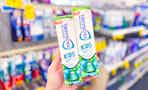 person holding 2 tubes of sensodyne kids toothpaste in an aisle